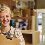 Portrait_Of_Female_Apprentice_With_Clipboard_Working_As_Carpenter_In_Furniture_Workshop