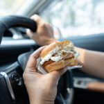 Asian_lady_holding_hamburger_to_eat_in_car,_dangerous_and_risk_an_accident.