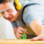 Konzentration bei der Arbeit Carpenter_working_on_an_electric_buzz_saw_cutting_some_boards,_he_is_wearing_safety_glasses_and_hearing_protection_for_workplace_safety