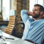 Work_done._Satisfied_young_bearded_businessman_leaning_back_with_hands_behind_head_and_relaxing_while_sitting_in_the_modern_office._Relax_concept._Workplace